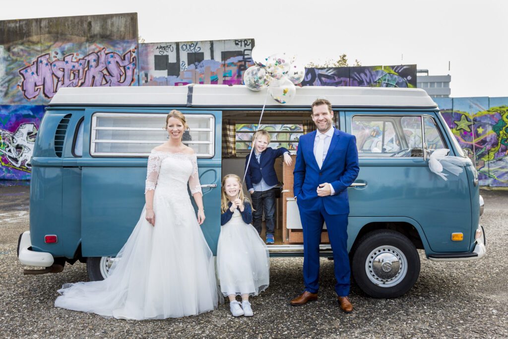 Bruidspaar staat met zoon en dochter vooreen Volkswagenbus.