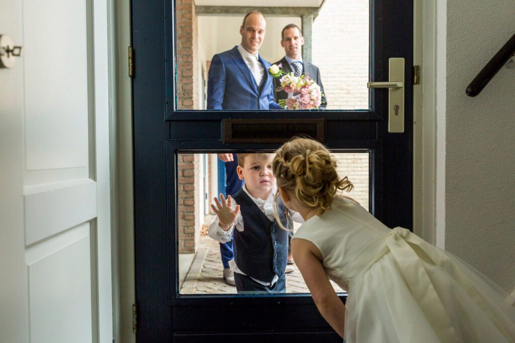 Bruidskinderen kijken naar elkaar door de voordeur.