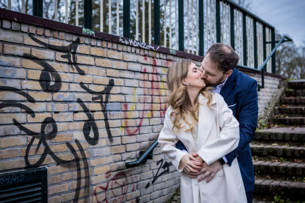 Bruid en bruidegom kussen elkaar voor een muur met graffiti.