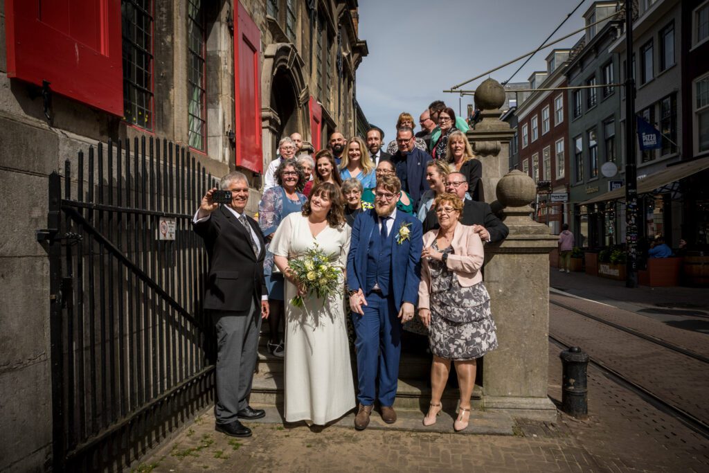 Vrienden en familie maken een selfie met het bruidspaar bij het Oude Stadhuis in Den Haag.