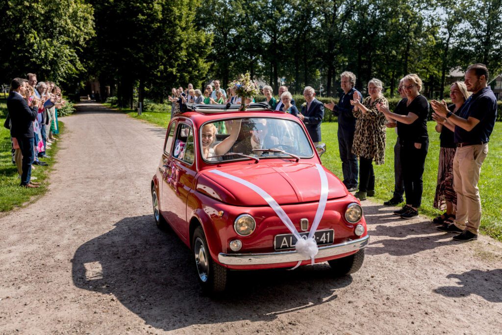 Bruidspaar komt op de trouwlocatie aanrijden in een Fiat 500.