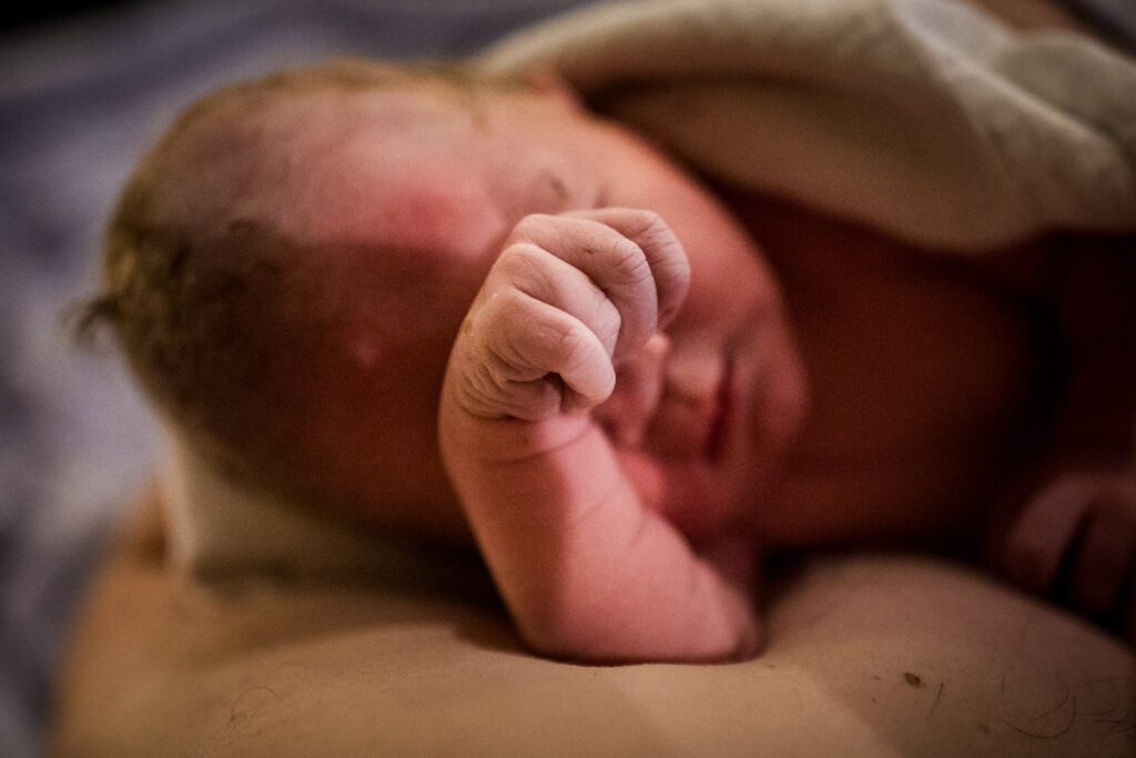 Pasgeboren baby houdt handje voor zijn gezicht