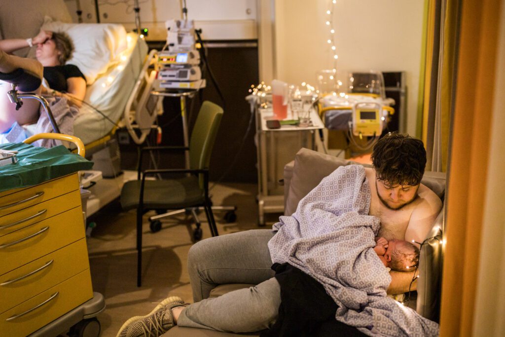 Man kijkt naar baby in zijn armen terwijl vrouw gehecht wordt