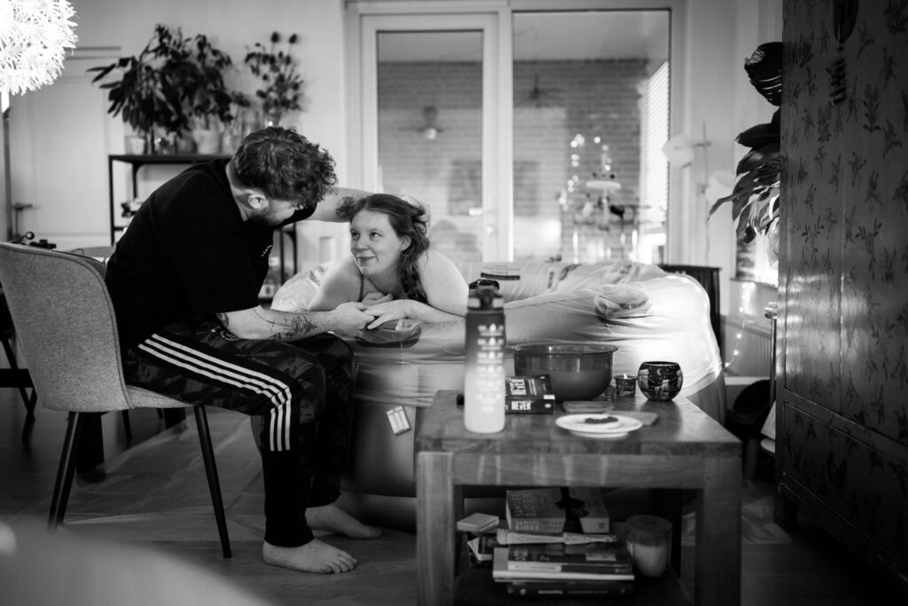 Man ondersteunt vrouw bij een badbevalling