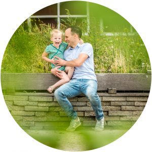 Vader en dochter worden gefotografeerd in een groene maar industriele setting.