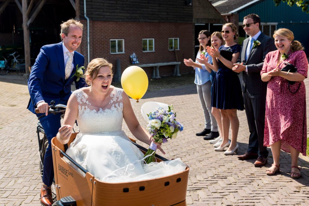 Bruidegom en bruid arriveren in de bakfiets bij Wijnhoeve de Heikant.