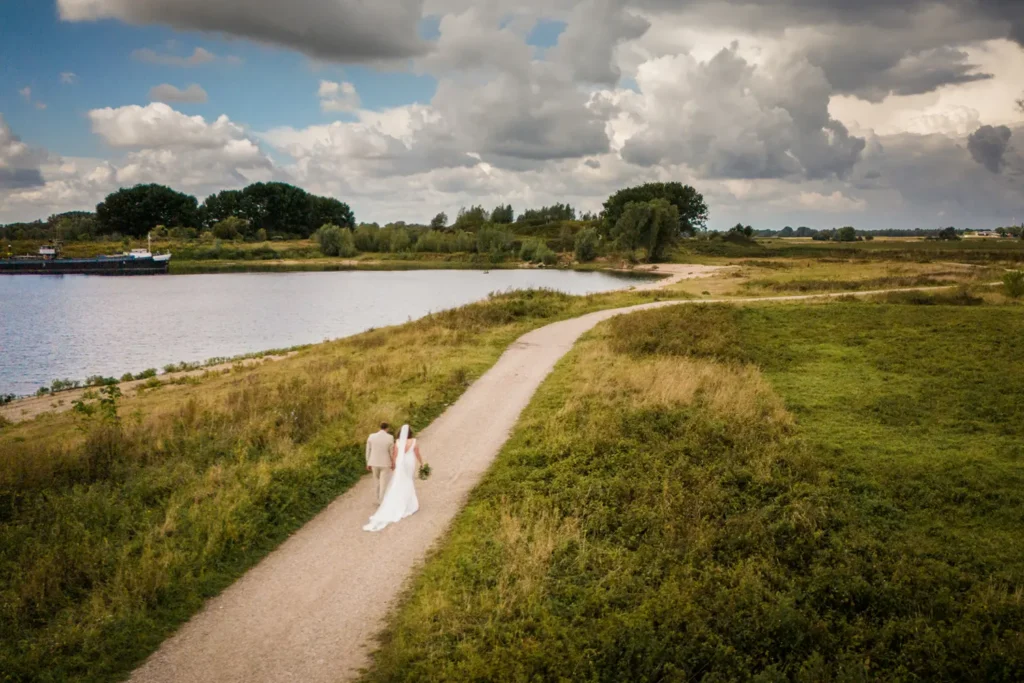 Drone-foto van het bruidspaar dat langs de dijk loopt.