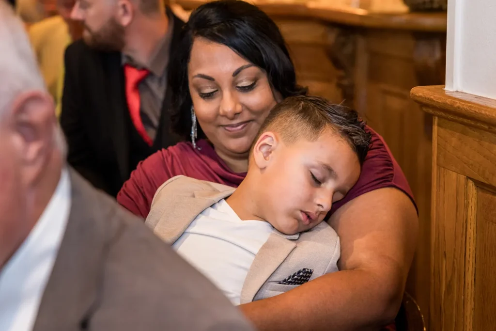 Jonge bruiloftsgast doet een dutje op schoot van z'n moeder.