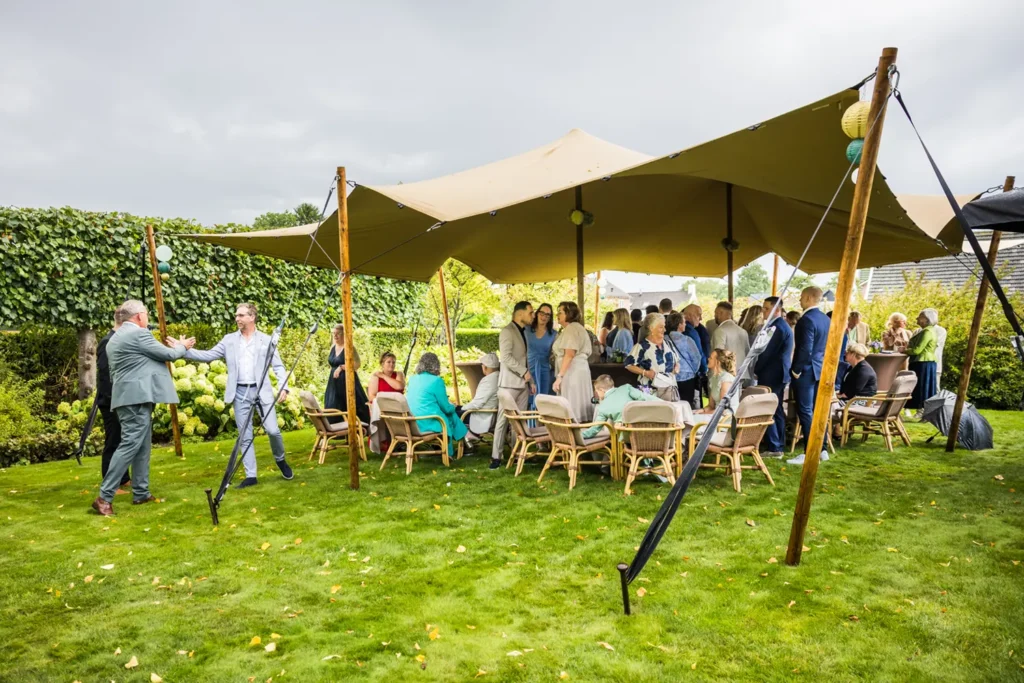 Bruiloftsgasten verzamelen onder de tent in de tuin.