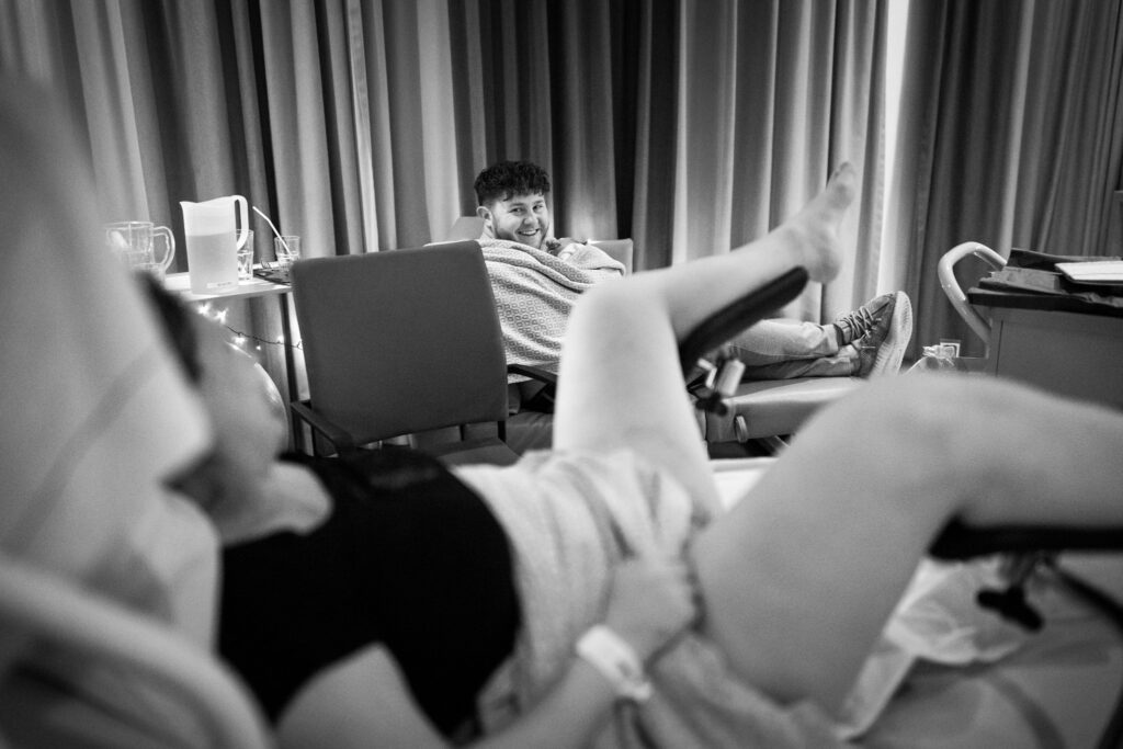 Man lacht naar zijn vrouw terwijl hij zijn pasgeboren zoon vasthoudt