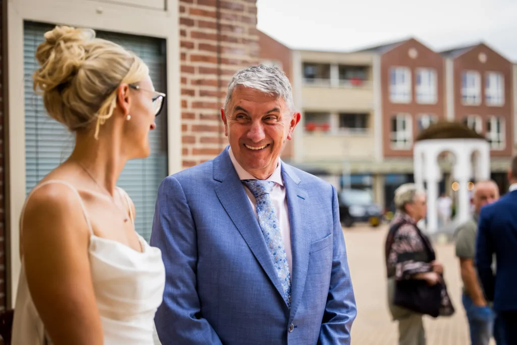 Vader van de bruid kijkt zijn dochter lachend aan.