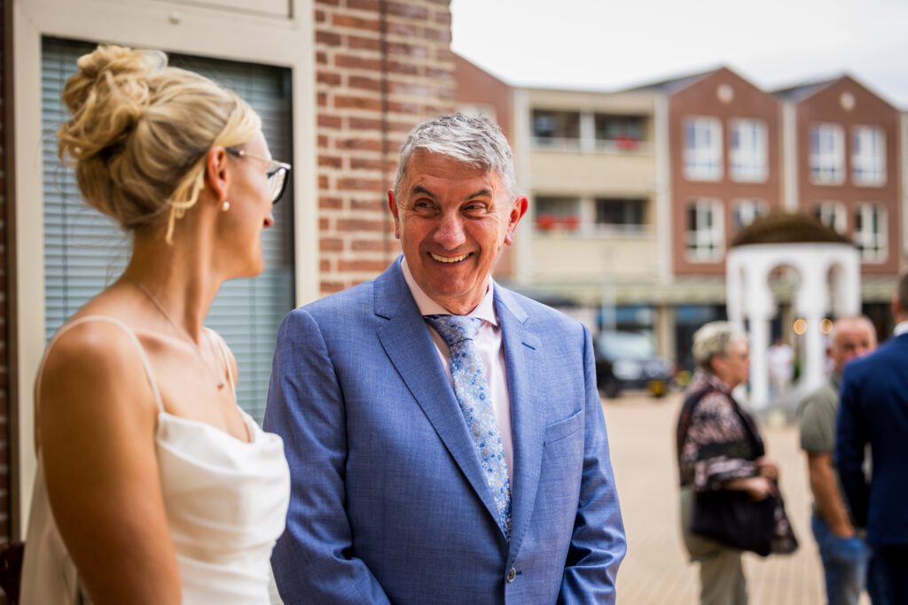 Vader van de bruid kijkt zijn dochter lachend aan.