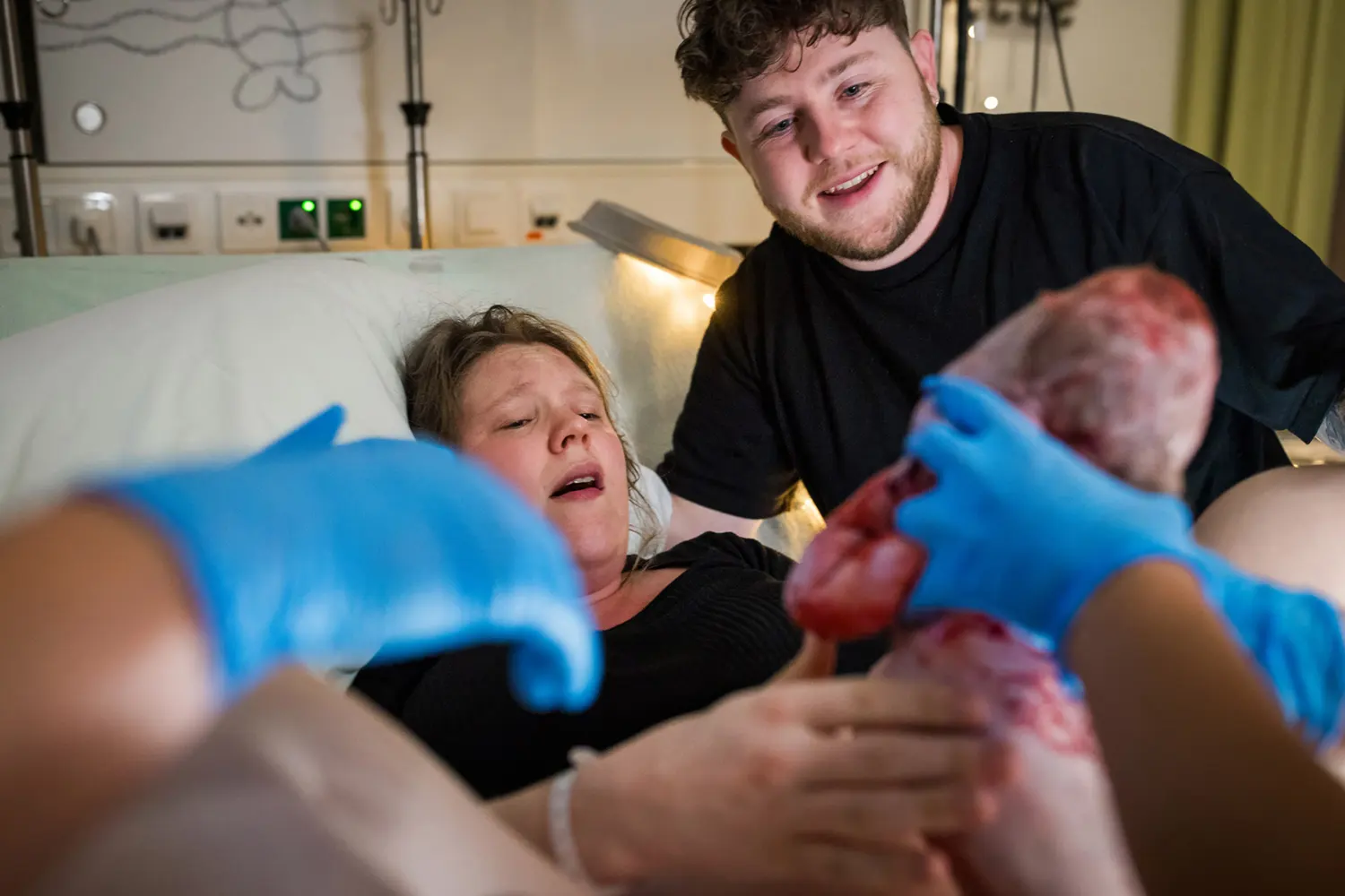 Moeder pakt haar kind aan tijdens de geboorte terwijl vader trots toekijkt.