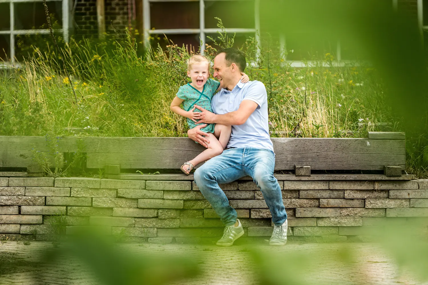 Vader en dochter lachen samen terwijl ze op een muurtje zitten.