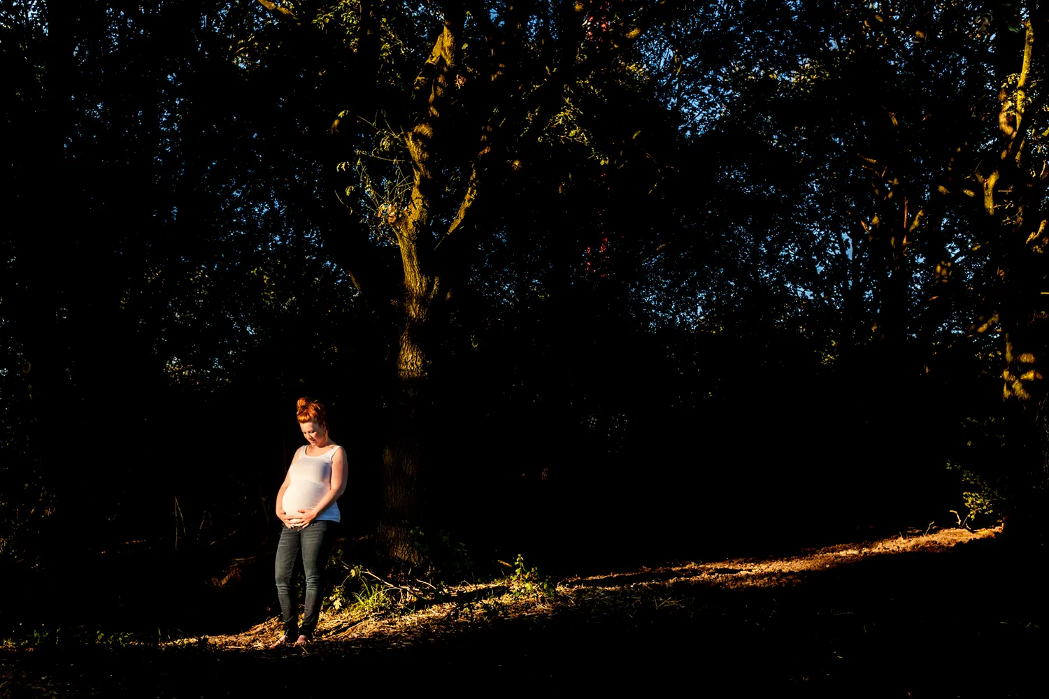 Zwangere vrouw staat in het licht van de ondergaande zon