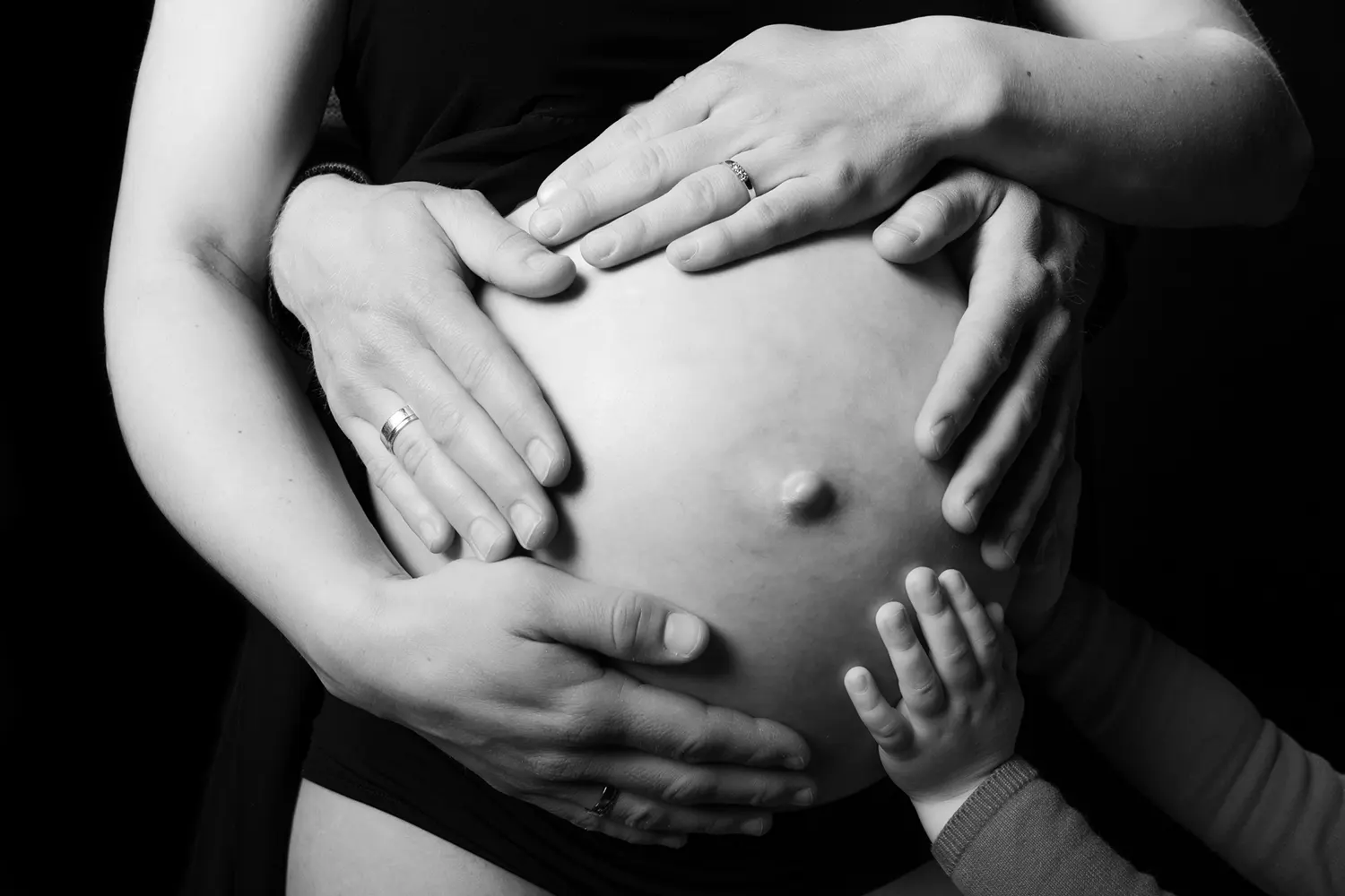 6 handen houden zwangere buik vast.